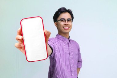 Sıradan gömlekli gülümseyen Asyalı genç adam beyaz arka planda boş akıllı telefon ekran modeli gösteriyor. Promosyon, dijital pazarlama ve reklam tasarımı için mükemmel..