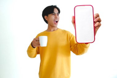 Genç adam elinde telefon ve fincanla gülümsüyor..