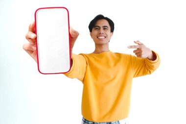 Heyecanlı Asyalı genç adam gülümserken boş bir akıllı telefon ekranını işaret ediyor, beyaz arka planda izole edilmiş, model, dijital promosyon ve çevrimiçi reklam için mükemmel..