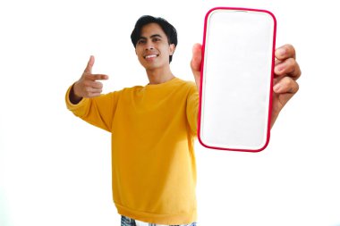 Heyecanlı Asyalı genç adam gülümserken boş bir akıllı telefon ekranını işaret ediyor, beyaz arka planda izole edilmiş, model, dijital promosyon ve çevrimiçi reklam için mükemmel..