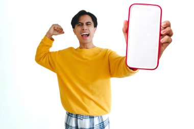 Heyecanlı Asyalı adam kameraya boş bir akıllı telefon ekranı tutarken ve gösterirken bağırıyor, beyaz arka planda izole edilmiş, reklam veya promosyon içeriği için mükemmel..