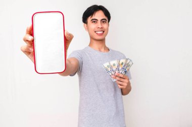Elinde para tutan ve beyaz arka planda izole edilmiş, reklam ya da promosyon için mükemmel olan boş bir akıllı telefon model ekranı gösteren mutlu Asyalı genç adam..