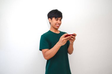 Mutlu Asyalı genç adam akıllı telefonuyla oyun oynuyor, beyaz arka planda izole edilmiş.