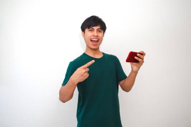Beyaz arka planda izole edilmiş kameraya bakarken akıllı telefondan mobil oyun oynayan mutlu Asyalı genç adam.