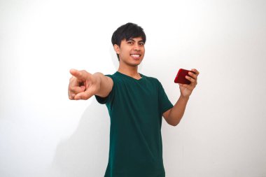 Beyaz arka planda izole edilmiş kameraya bakarken akıllı telefondan mobil oyun oynayan mutlu Asyalı genç adam.