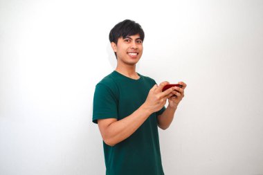 Mutlu Asyalı genç adam akıllı telefonuyla oyun oynuyor, beyaz arka planda izole edilmiş.