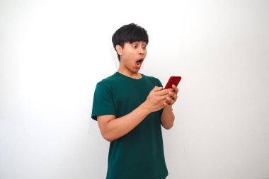 Zeki telefonuna bakan Asyalı genç bir adamın portresi. Şaşırmış mutlu bir ifadeyle. Parlak bir arka planda izole edilmiş.