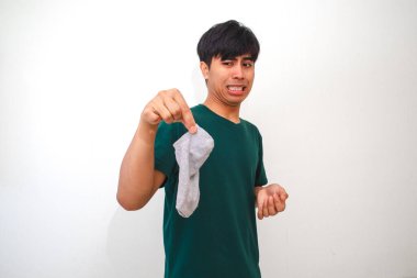 İzole edilmiş beyaz arka planda pis kokulu çoraplar tutan Asyalı genç adam, reklam için stüdyo yaşam tarzı konseptinde komik bir tepki gösteriyor.