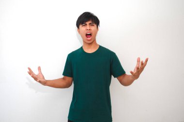 Asyalı genç bir adamın portresi kızgın bir yüz ifadesi ve el hareketiyle stüdyoda kameraya bakıyor, duygusal reklam için mükemmel.