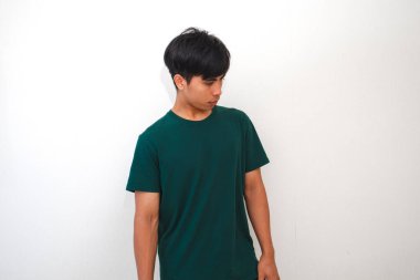 Asyalı genç bir adam, izole edilmiş beyaz bir arka planda yorgun bir hareketle ayakta duruyor ve aşağı bakıyor. İş, yaşam tarzı ve reklam kavramları için mükemmel..