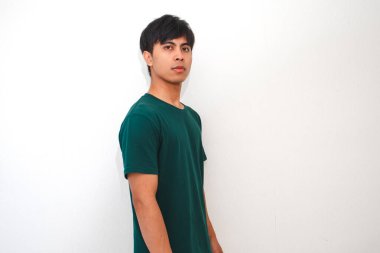 Genç Asyalı adam dikilip kameraya bakıyor. İzole edilmiş beyaz bir arka planda nötr bir ifadeyle.