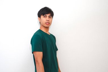 Genç Asyalı adam dikilip kameraya bakıyor. İzole edilmiş beyaz bir arka planda nötr bir ifadeyle.
