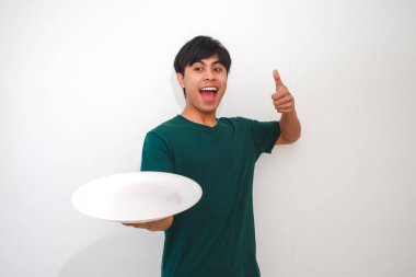 Asyalı genç adam boş bir yemek tabağı gösterirken beyaz arka planda izole edilmiş, yemek reklamları, promosyonlar veya yaşam tarzı içeriği için mükemmel bir jest yapıyor.