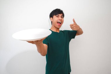 Asyalı genç adam boş bir yemek tabağı gösterirken beyaz arka planda izole edilmiş, yemek reklamları, promosyonlar veya yaşam tarzı içeriği için mükemmel bir jest yapıyor.