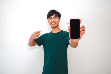 Akıllı telefonu boş ekranla gösteren mutlu Asyalı genç adam izole edilmiş beyaz arka planda heyecanla gülümsüyor. Teknoloji, promosyon ve reklam temaları için mükemmel.