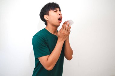 Genç Asyalı bir adam burnunu ve ağzını kapatırken mendile hapşırıyor, temiz beyaz bir arka planda izole edilmiş. Sağlık, hijyen ya da reklam kavramları için mükemmel.