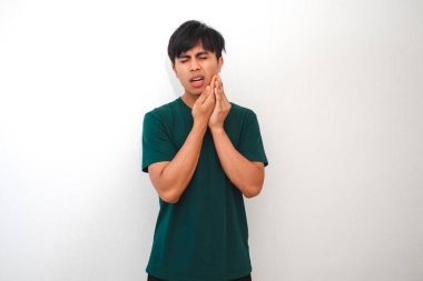 Acı dolu bir ifadeyle çenesine dokunan genç bir Asyalı, muhtemelen diş ağrısı yüzünden, beyaz arka planda izole edilmiş. Diş bakımı, sağlık ve tıbbi reklamlar için mükemmel.
