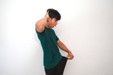 Asyalı adam pantolonunun içinde cinsel organını dikizliyor. İzole edilmiş beyaz arka planda tuhaf bir şok ifadesi gösteriyor.