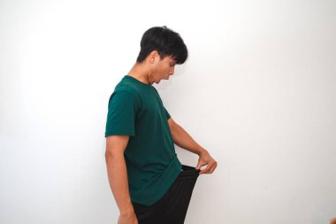 Asyalı adam pantolonunun içinde cinsel organını dikizliyor. İzole edilmiş beyaz arka planda tuhaf bir şok ifadesi gösteriyor.