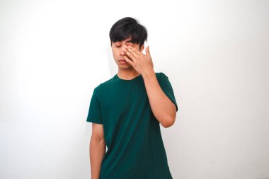 Genç Asyalı adam elleriyle gözlerini ovuşturuyor, yorgun ya da stresli görünüyor, izole beyaz arka plana karşı duruyor. Yorgunluk, tükenme ya da günlük hayatta uykusuzluk kavramı