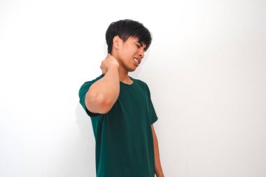 Genç Asyalı bir adam acı dolu bir ifadeyle boynuna dokunuyor, izole beyaz bir arka plana karşı duruyor. Sağlık, stres ve tıbbi reklamlar için uygundur