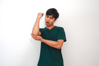 Dirsek ağrısından muzdarip genç bir Asyalı, beyaz arka planda, kolunu tutarken acı dolu bir ifade sergiliyor. Sağlık, tıbbi veya reklam içeriği için mükemmel