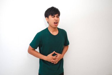 Genç Asyalı bir adam midesi ağrıyan bir mide ağrısı yaşıyor. Beyaz bir arka plan karşısında duruyor. Sağlık ve tıbbi reklam kavramları için mükemmel.