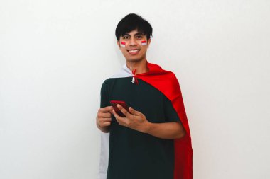 Beyaz izole edilmiş arka planda elinde bayrak ve akıllı telefon tutan gülümseyen Endonezyalı adam, bağımsızlık kutlamaları, reklamcılık ve vatanseverlik içeriği için mükemmel..