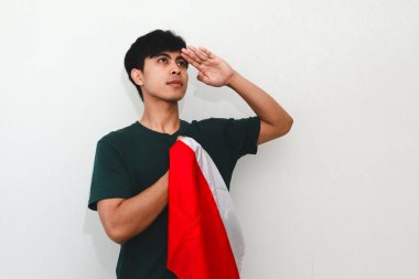 Endonezyalı adam ulusal bayrağı beyaz bir arka planda tutarken selamlıyor, bağımsızlık günü kutlamaları ve vatansever reklamlar için mükemmel..