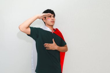 Endonezyalı adam ulusal bayrağı beyaz bir arka planda tutarken selamlıyor, bağımsızlık günü kutlamaları ve vatansever reklamlar için mükemmel..