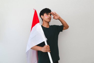 Endonezyalı adam ulusal bayrağı beyaz bir arka planda tutarken selamlıyor, bağımsızlık günü kutlamaları ve vatansever reklamlar için mükemmel..