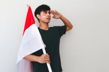 Endonezyalı adam ulusal bayrağı beyaz bir arka planda tutarken selamlıyor, bağımsızlık günü kutlamaları ve vatansever reklamlar için mükemmel..