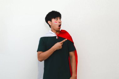 Heyecanlı Endonezyalı bir adam elinde bir bayrak, boş fotokopi alanını işaret ediyor, beyaz arka planda izole edilmiş, reklam ve kutlama kavramları için mükemmel..