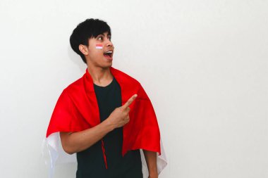 Heyecanlı Endonezyalı bir adam elinde bir bayrak, boş fotokopi alanını işaret ediyor, beyaz arka planda izole edilmiş, reklam ve kutlama kavramları için mükemmel..