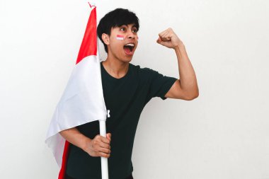 Heyecanlı genç Asyalı adam Endonezya 'nın Bağımsızlık Günü' nü 17 Ağustos 'ta kutluyor. Elinde Endonezya bayrağını tutarak ve beyaz arka planda izole edilmiş yumruğunu sıkarak.