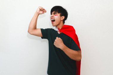 Heyecanlı genç Asyalı adam Endonezya 'nın Bağımsızlık Günü' nü 17 Ağustos 'ta kutluyor. Elinde Endonezya bayrağını tutarak ve beyaz arka planda izole edilmiş yumruğunu sıkarak.