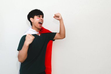 Heyecanlı genç Asyalı adam Endonezya 'nın Bağımsızlık Günü' nü 17 Ağustos 'ta kutluyor. Elinde Endonezya bayrağını tutarak ve beyaz arka planda izole edilmiş yumruğunu sıkarak.