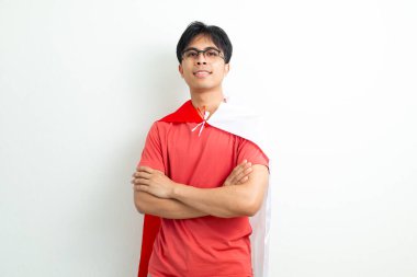 Endonezyalı genç bir adam, Endonezya bayrağını tutarak güvenle gülümsüyor, kollarını kavuşturup, 17 Ağustos 'taki Bağımsızlık Gününü kutluyor.