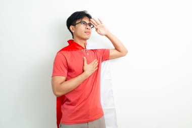 Endonezyalı gururlu genç bir adam Endonezya bayrağını tutuyor ve el ele selamlıyor, Bağımsızlık Günü 'nü parlak bir arka planda vatansever bir ifadeyle kutluyor.