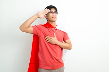 Endonezyalı gururlu genç bir adam Endonezya bayrağını tutuyor ve el ele selamlıyor, Bağımsızlık Günü 'nü parlak bir arka planda vatansever bir ifadeyle kutluyor.