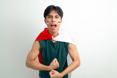 Bağımsızlık Günü 'nü kutlayan heyecanlı Endonezyalı genç adam, izole edilmiş arka planda gururlu bir ifadeyle elinde ulusal bayrak tutarken güçlü bir kol hareketi gösteriyor.