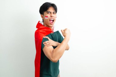 Bağımsızlık Günü 'nü kutlayan heyecanlı Endonezyalı genç adam, izole edilmiş arka planda gururlu bir ifadeyle elinde ulusal bayrak tutarken güçlü bir kol hareketi gösteriyor.