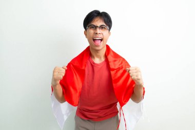 Heyecanlı Endonezyalı genç bir adam elinde ulusal bayrak ve sıkılmış bir yumrukla bağırıyor, Bağımsızlık Günü 'nü ruhuyla kutluyor, beyaz arka planda izole edilmiş bir şekilde.