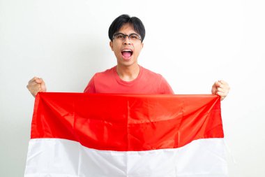 Heyecanlı Endonezyalı genç bir adam elinde ulusal bayrak ve sıkılmış bir yumrukla bağırıyor, Bağımsızlık Günü 'nü ruhuyla kutluyor, beyaz arka planda izole edilmiş bir şekilde.