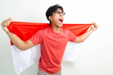 Heyecanlı Endonezyalı genç bir adam elinde ulusal bayrak ve sıkılmış bir yumrukla bağırıyor, Bağımsızlık Günü 'nü ruhuyla kutluyor, beyaz arka planda izole edilmiş bir şekilde.