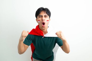 Heyecanlı Endonezyalı genç bir adam elinde ulusal bayrak ve sıkılmış bir yumrukla bağırıyor, Bağımsızlık Günü 'nü ruhuyla kutluyor, beyaz arka planda izole edilmiş bir şekilde.