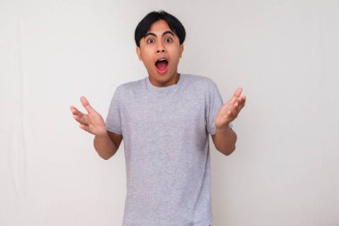 Heyecanlı genç Asyalı adam beyaz arka planda izole edilmiş, hayret verici bir yüz ifadesiyle kameraya bakıyor. Reklam ve tanıtım içeriği için mükemmel.