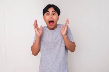 Heyecanlı genç Asyalı adam beyaz arka planda izole edilmiş, hayret verici bir yüz ifadesiyle kameraya bakıyor. Reklam ve tanıtım içeriği için mükemmel.