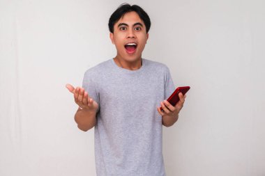 Heyecanlı Asyalı genç adam elinde akıllı bir telefon tutuyor. Yüzünde hayret verici bir ifade var. Beyaz arka planda izole edilmiş. Teknoloji, reklam ya da online tanıtım temaları için mükemmel