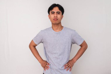 Belini tutan ve beyaz izole bir arka planda kızgın bir ifadeyle kameraya bakan Asyalı genç bir adamın portresi. Duygular ve tutumlar için mükemmel.